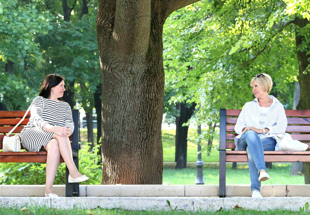 Two women having a conversation across a divide of 2 benches